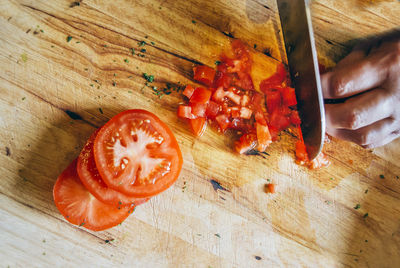 Cropped hand of person cutting tomatoes on table