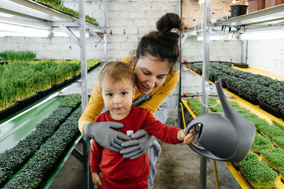Woman with baby boy working on the indoor farm, planting microgreens. choosing seeds and watering