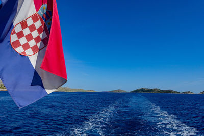 Scenic view of flag on sea against clear blue sky