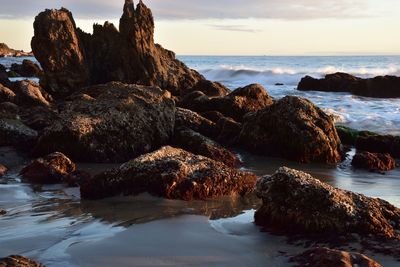 Rocks on beach against sky during sunset