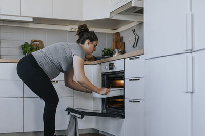 Pregnant woman putting dish in oven
