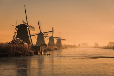 Traditional windmill on shore against sky during sunset