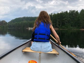 Rear view of woman boating in lake against cloudy sky