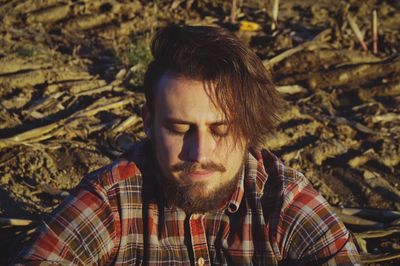 Young man with eyes closed sitting on field