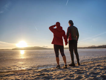 Fitnes couple man and woman. winter landscape with sun at horizon. frozen river makes reflection.