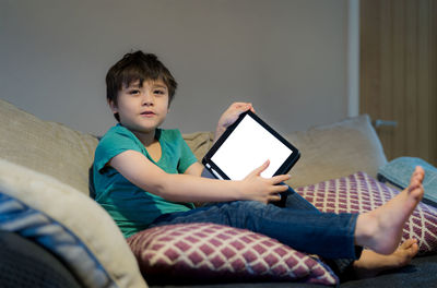 Portrait of cute boy holding digital tablet sitting on sofa at home