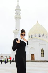 Young woman wearing traditional clothing standing against mosque