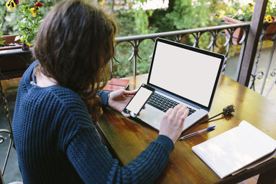 Young woman sitting on balcony using laptop and smart phone