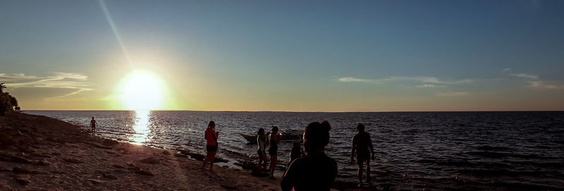 Silhouette people on beach against sky during sunset