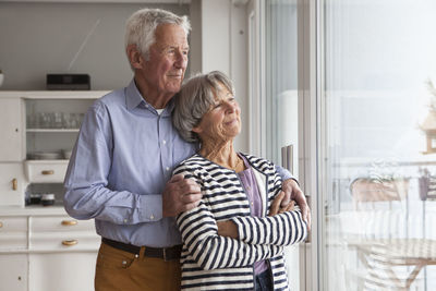 Portrait of confident senior couple looking through window at home