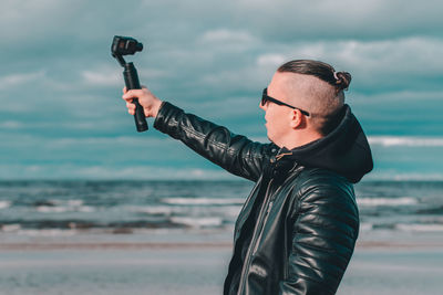 Young man blogging while standing at beach