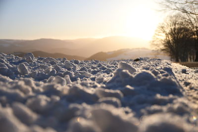 Surface level of snow covered land against sky during sunset