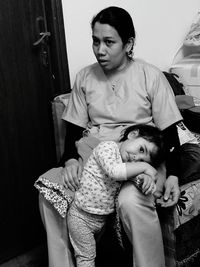 Mother sitting with daughter on chair at home