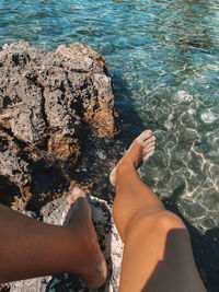 Low section of people relaxing on rock by sea