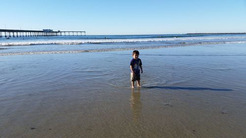 Boy standing at beach against clear sky