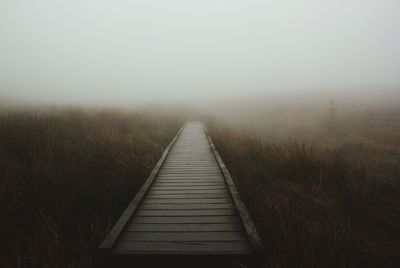 Boardwalk in foggy weather against sky