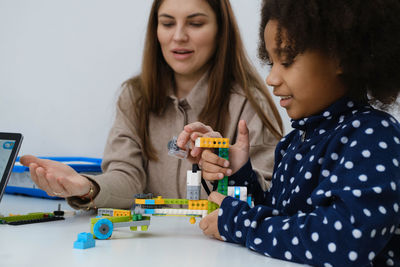 Multiethnic kids at stem lesson constructing robot in classroom with woman teacher children making