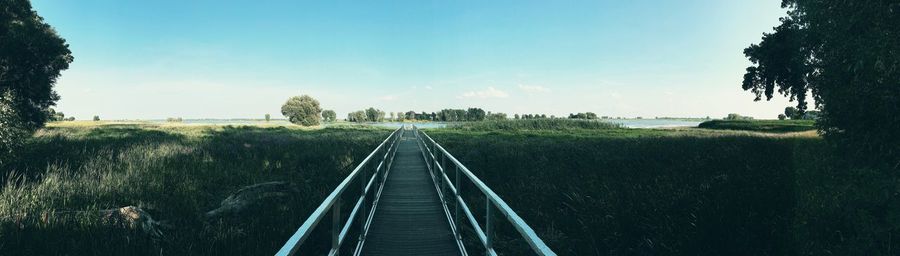 Footbridge leading towards river against sky