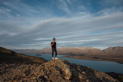 Full length of man standing on cliff against cloudy sky