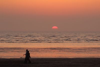 Men in sea against sunset sky