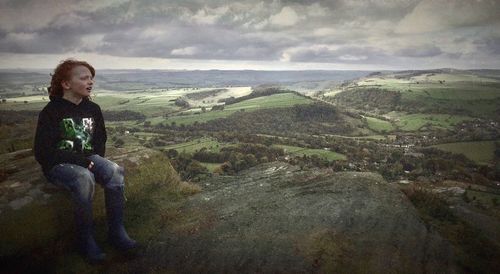 Man sitting on rock against sky