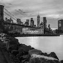 Bridge over river by buildings against sky in city