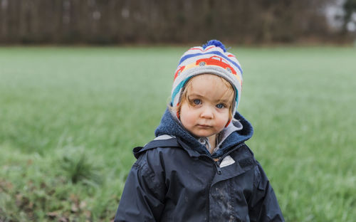 Portrait of cute girl wearing warm clothing standing on grassy field in park