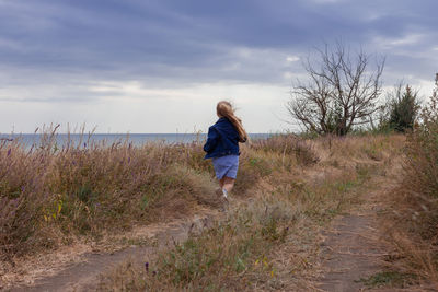 Blond long hair child girl in denim jacket walks on sea landscape. travelling hiking running outdoor