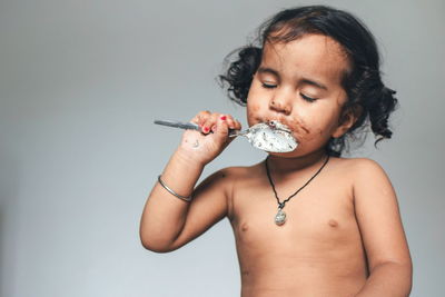 Portrait of shirtless girl eating food against gray background
