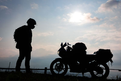 Silhouette man standing by bicycle against sky during sunset