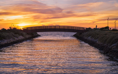 Bridge over river against orange sky