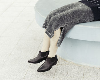 Low section of woman wearing black shoes sitting on retaining wall