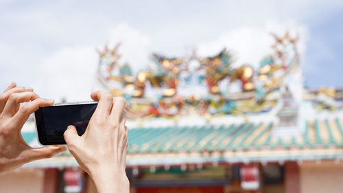 Tourist using a smartphone taking photo of a chinese shrine roof.