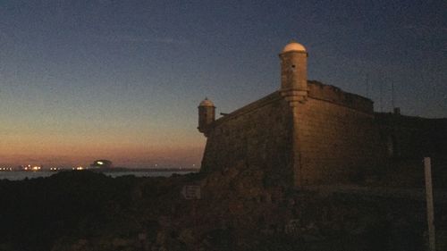 Illuminated tower by sea against sky at dusk