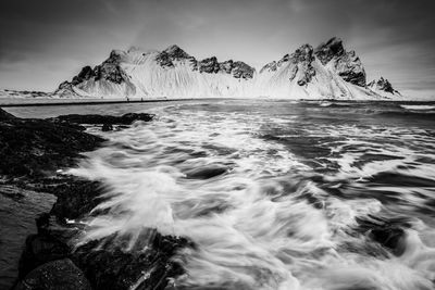 Scenic view of sea by snowcapped mountain against sky