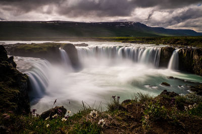 Scenic view of waterfall against cloudy sky