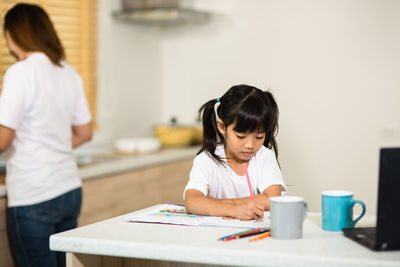 Girl painting on table with mother in background