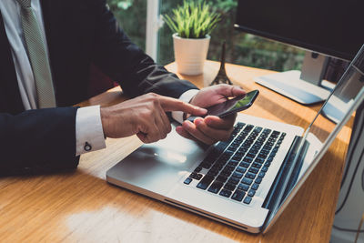 Midsection of businessman using phone by laptop on table