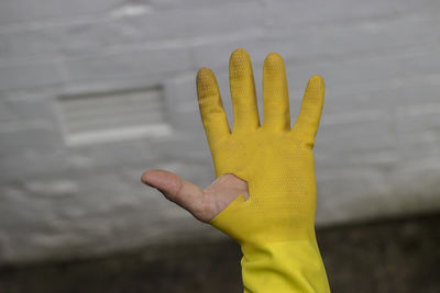 Close-up of hand holding yellow leaf against wall