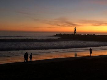 Silhouette people standing on beach against sky during sunset