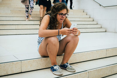 Young woman using phone while sitting on steps