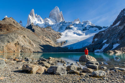 Rear view of person on snowcapped mountain by lake against sky