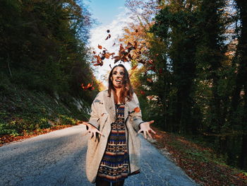 Portrait of smiling young woman standing on road against trees