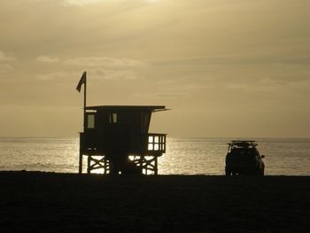 Silhouette hut on beach against sky during sunset