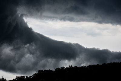 Low angle view of silhouette trees against storm clouds