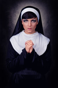 Portrait of nun praying while standing against black background