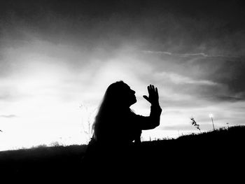 Side view of woman with arms raised against sky during sunset