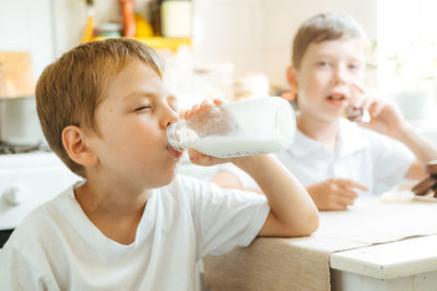 A boy is drinking milk from a bottle in the kitchen at home. morning breakfast with milk. 