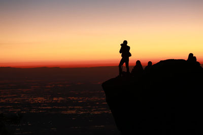 Silhouette people on rock against sky during sunset