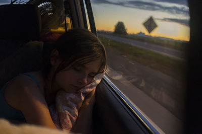 A young girl sleeping in the back of a car with her head on the window